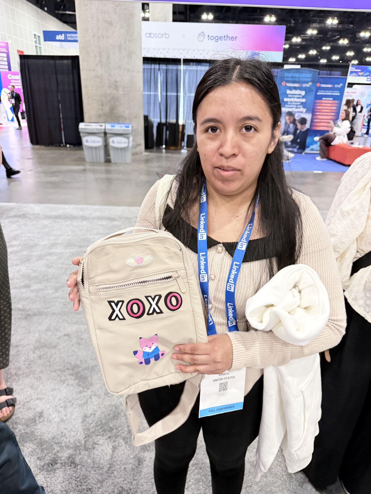 Young woman proudly displays a custom branded cream crossbody bag with embroidered design at a conference